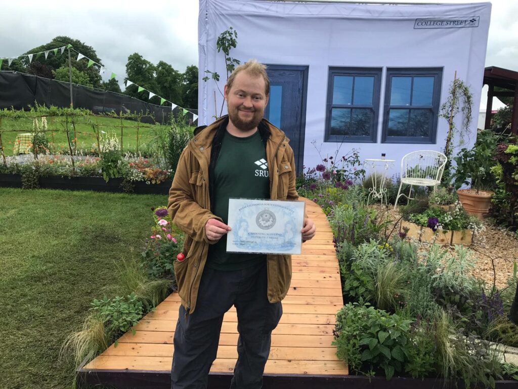 John Thoumire standing his show garden called 'Bayet' at Gardening Scotland - holding certificate